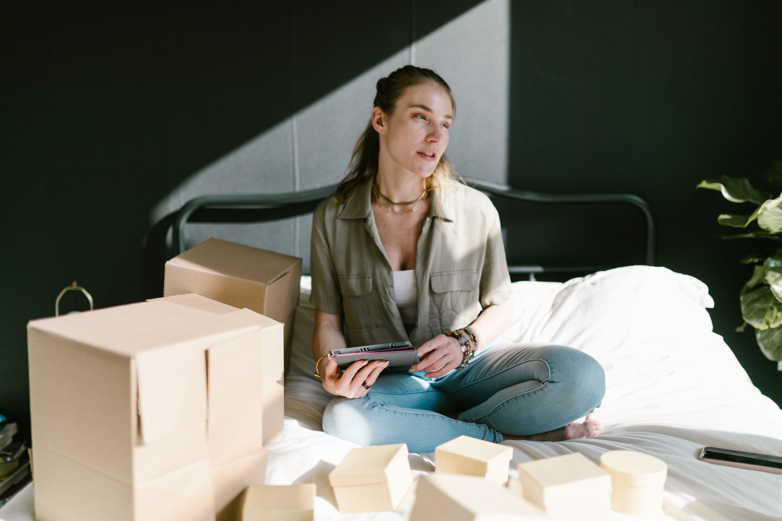 Young woman planning her startup business in bed with boxes and tablet.